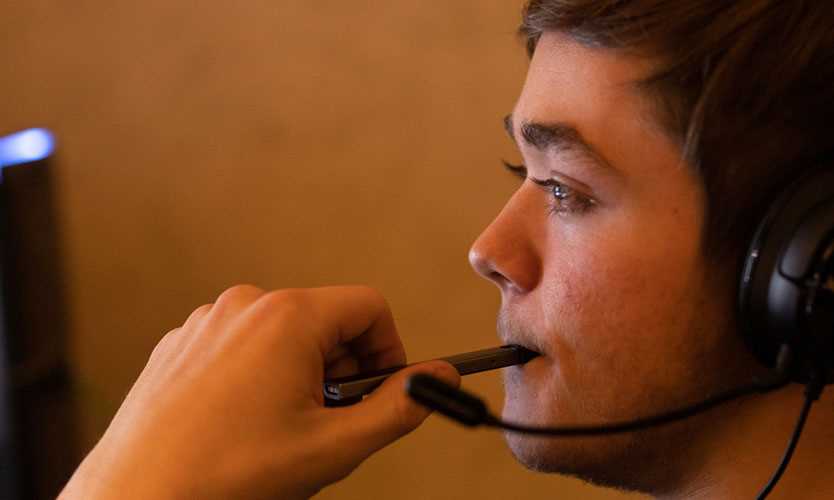 A teen vapes while playing video games.